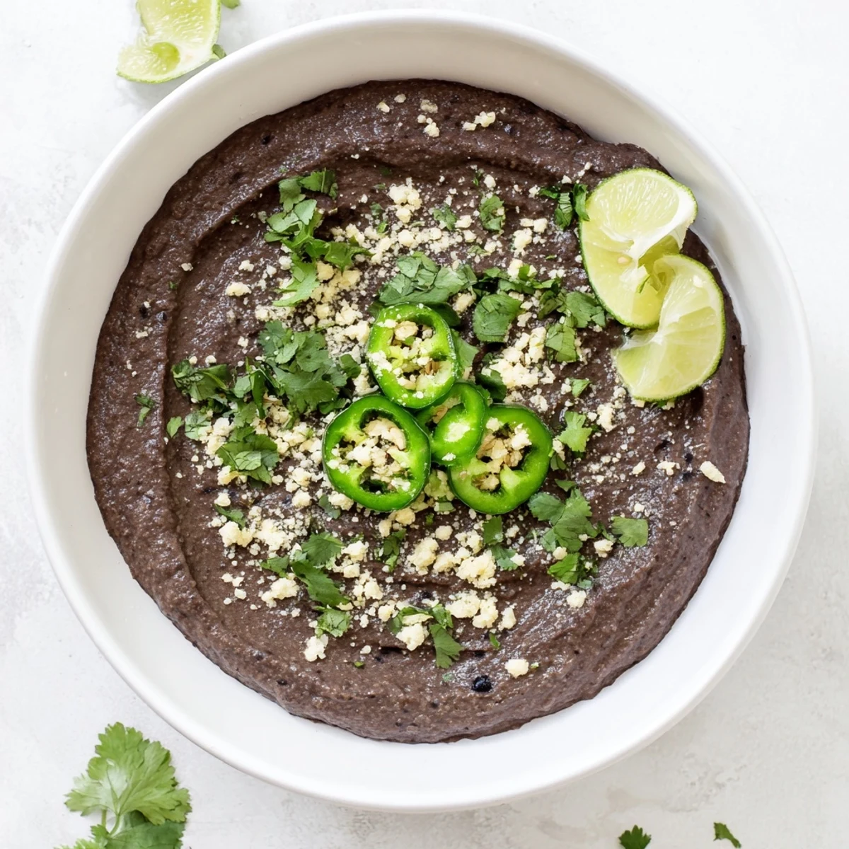Creamy Spicy Black Bean Dip in a rustic bowl, garnished with fresh cilantro and lime wedges for a zesty party appetizer.