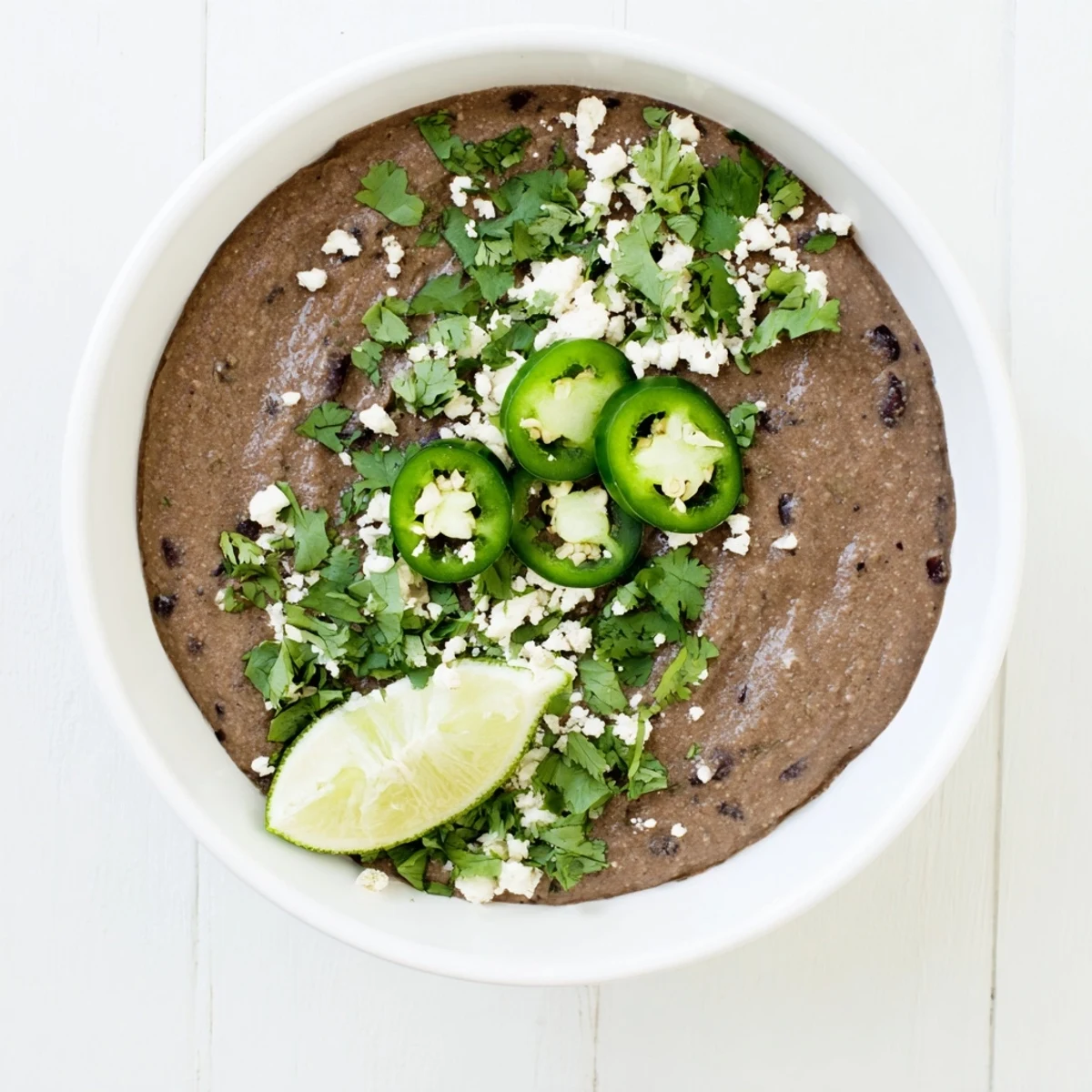 Vibrant bowl of homemade Spicy Black Bean Dip surrounded by crunchy tortilla chips and colorful veggie sticks for dipping.