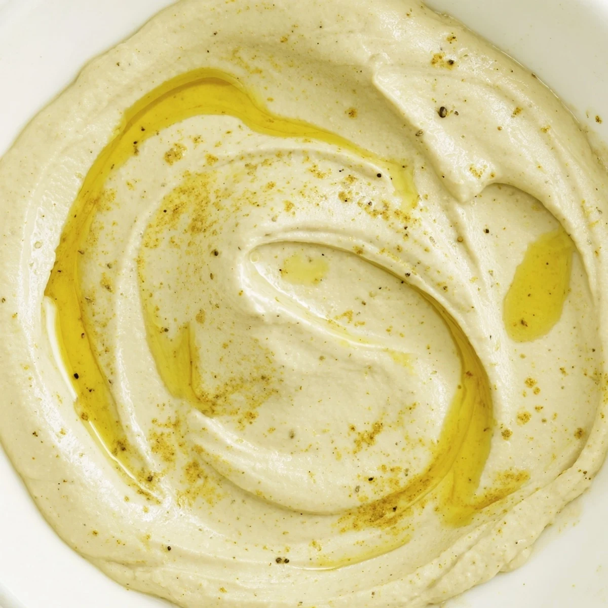 Creamy golden chickpea curry paste swirls in a rustic bowl, topped with a drizzle of olive oil and a sprinkle of curry powder for dipping.