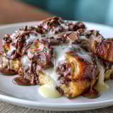 Warm chocolate croissant bread pudding baked to golden perfection, topped with powdered sugar and fresh berries for a delightful treat.