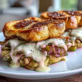 Miniature Hot Brown sandwiches featuring layers of turkey, tomatoes, and crispy bacon smothered in rich cheese sauce on golden slider buns.  