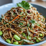 Cold sesame noodles with shredded carrots, cucumber, and green onions, drizzled in a tangy ginger dressing and garnished with sesame seeds.
