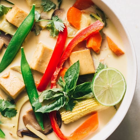 Steaming bowl of Thai Green Curry Coconut Soup, garnished with vibrant cilantro and lime wedges, ready to savor.