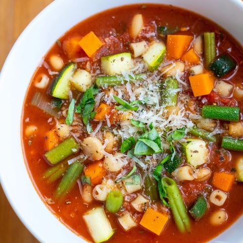 A steaming bowl of vibrant Tomato Basil Minestrone, garnished with fresh basil and Parmesan.