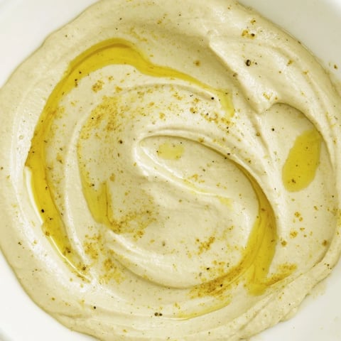 Creamy golden chickpea curry paste swirls in a rustic bowl, topped with a drizzle of olive oil and a sprinkle of curry powder for dipping.