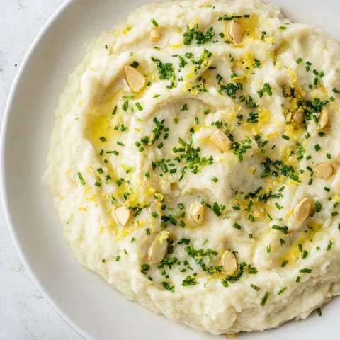 This vibrant photo shows a bowl of homemade cauliflower mash, enhanced with fresh herbs and lemon zest.