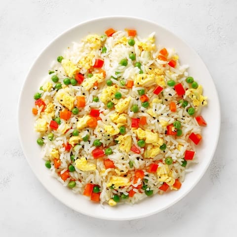 A hot wok steams with tender peas, carrots, and fluffy grains of Egg Fried Rice garnished with scallions.