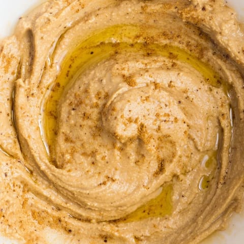 This vegan chickpea curry paste is garnished with fresh cilantro and served alongside crisp vegetable sticks and warm naan bread for scooping.