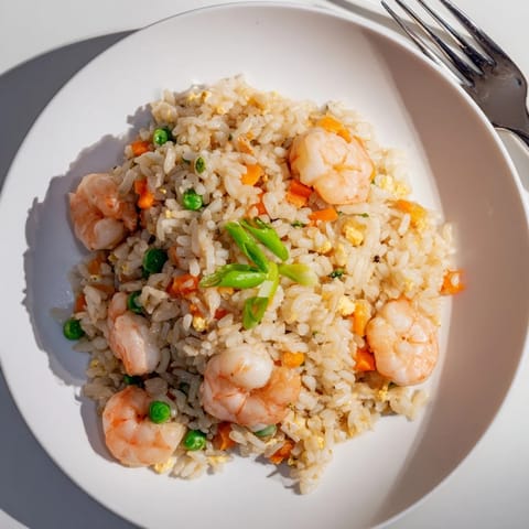 A close-up of fluffy jasmine rice tossed with succulent shrimp, crisp peas, and carrots, garnished with fresh spring onions and lime wedges.  