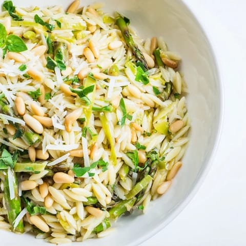 A bright bowl of Asparagus Lemon Orzo Salad topped with shaved Parmesan and golden toasted pine nuts, perfect for a sunny spring picnic.