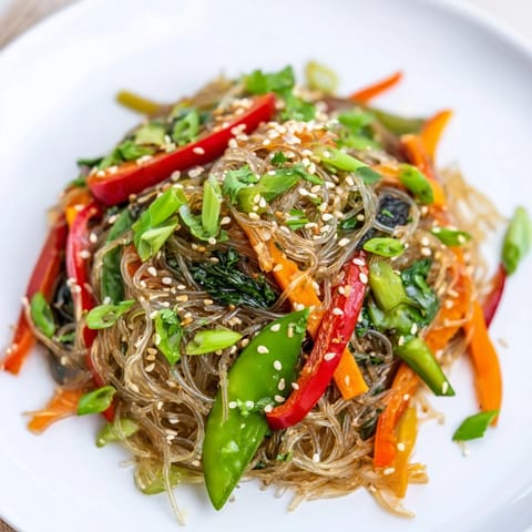Quick Kelp Noodle Stir-Fry topped with sesame seeds and lime wedges, showcasing vibrant red peppers and wilted spinach in a skillet.