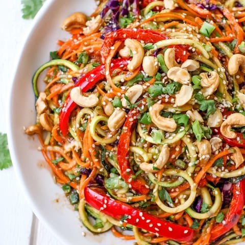 Vibrant raw vegetable noodle salad with red cabbage, cucumber, and bell pepper, topped with toasted sesame seeds for extra crunch.  