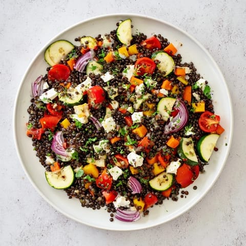 Black Lentil Salad plated with roasted veggies, cherry tomatoes, and crumbled feta on a rustic board.  
