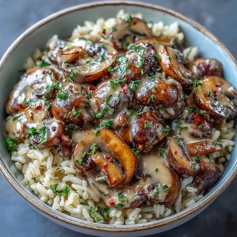 A hearty bowl of Vegan Mushroom Stroganoff over fluffy brown rice, with a drizzle of olive oil and herbs.