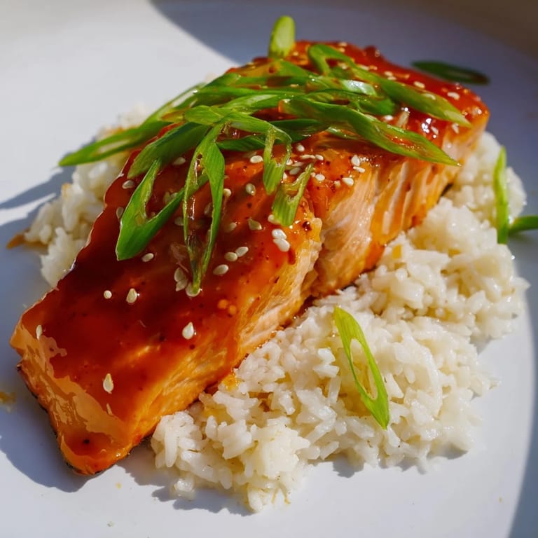 The baked Sticky Orange Salmon, caramelized and tender, is served with a vibrant scallion garnish and rice.
