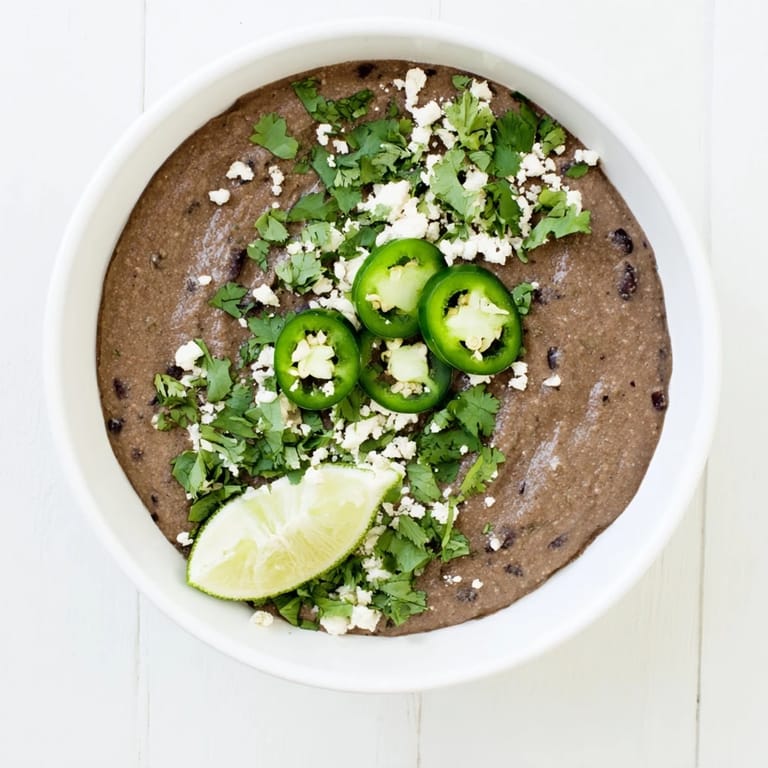 Vibrant bowl of homemade Spicy Black Bean Dip surrounded by crunchy tortilla chips and colorful veggie sticks for dipping.