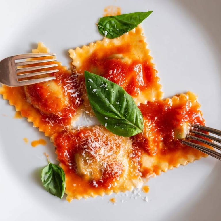 Spinach ricotta ravioli on a plate with rich red sauce, fresh basil, and grated cheese.