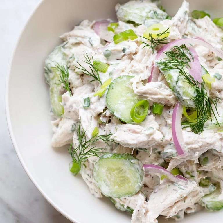 Freshly made creamy cucumber chicken salad garnished with green onions and dill, ready to serve on a rustic table.