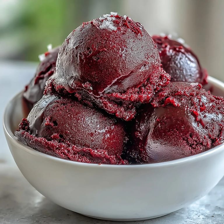 Lush Black Currant Sorbet is garnished with fresh mint and a drizzle of honey, served in a rustic white bowl.