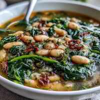 A bowl of Tuscan white bean and spinach soup with creamy beans and vibrant greens in a savory herb-infused broth.